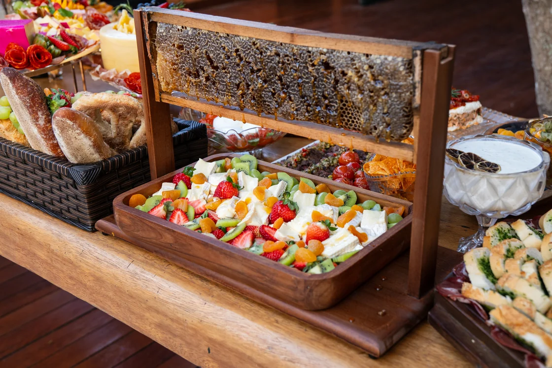 Favo de mel, queijos e frutas em travessas sobre uma mesa de buffet