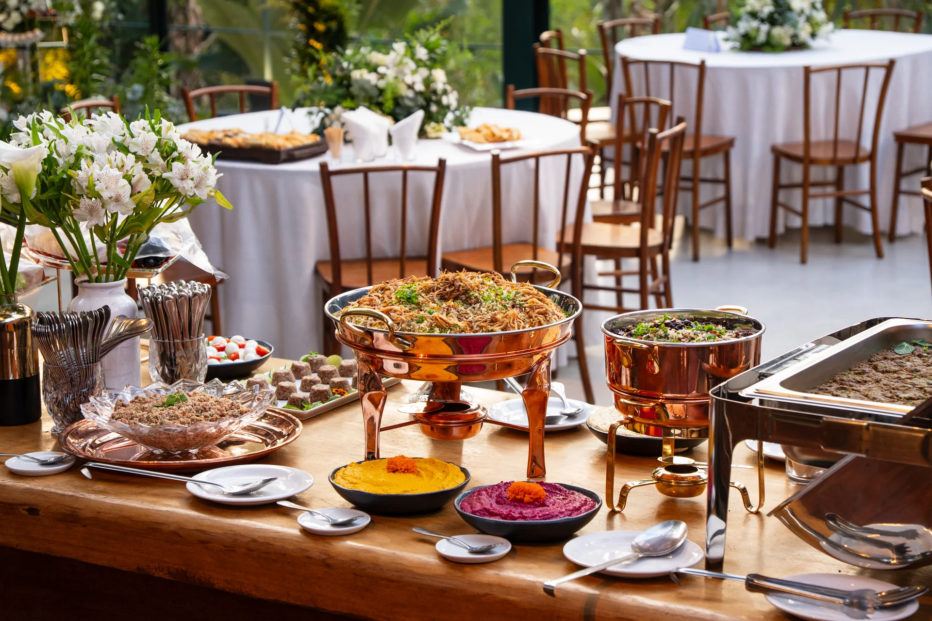 Mesa de buffet montada com recipientes de cobre, travessas e flores