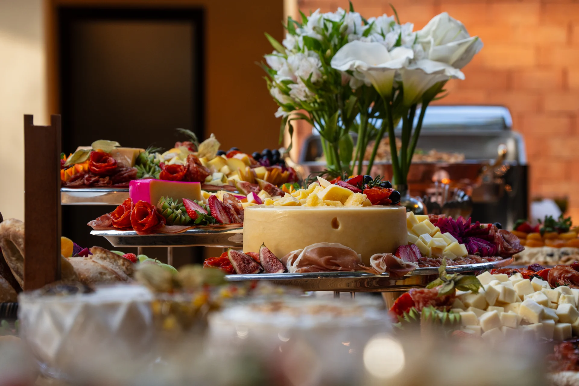 Mesa de buffet com queijos, frutas, frios e um arranjo de flores brancas